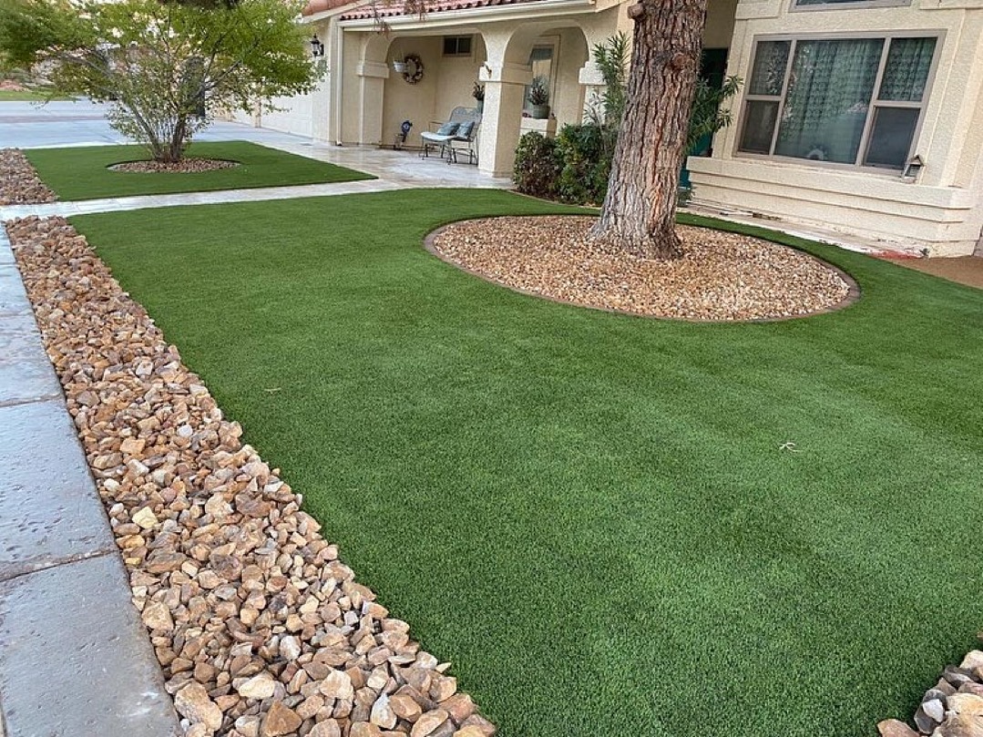 A landscaped area with artificial grass and rocks positioned in front of a residential house